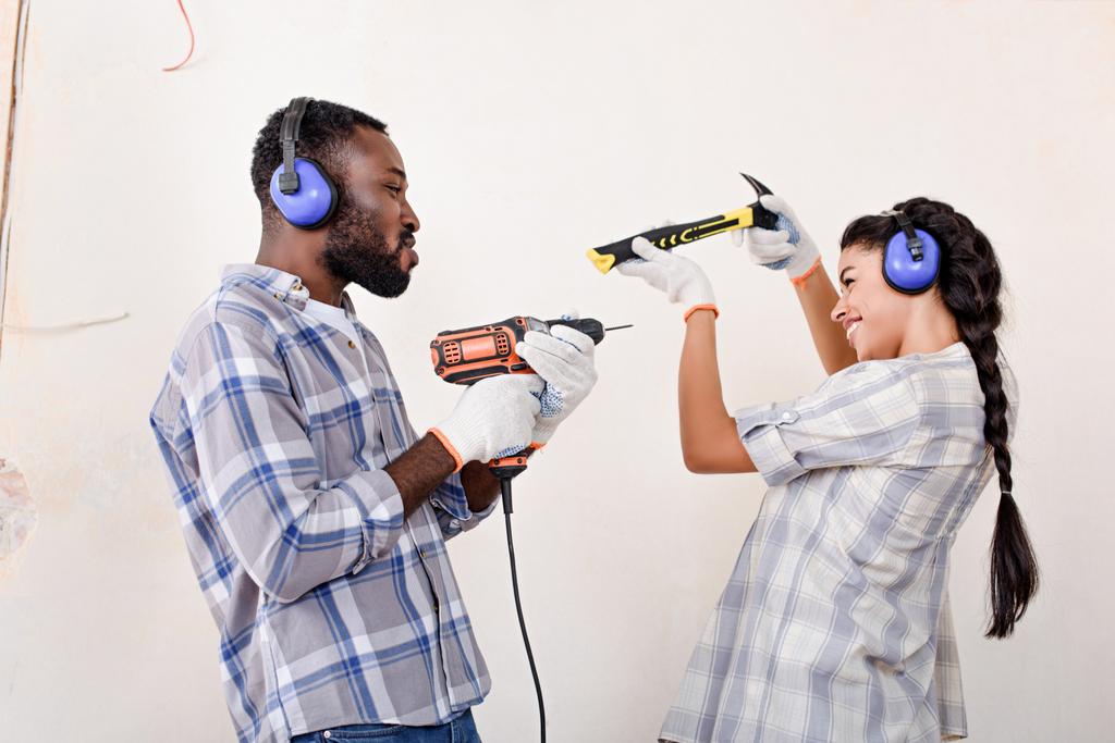 vista lateral do jovem casal brincalhão se divertindo com martelo e broca ao fazer a renovação de casa
 - Foto, Imagem