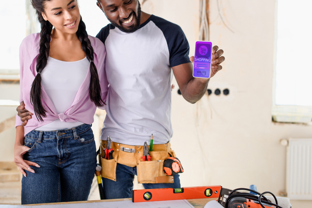 smiling couple holding smartphone with shopping app on screen during renovation - Photo, Image