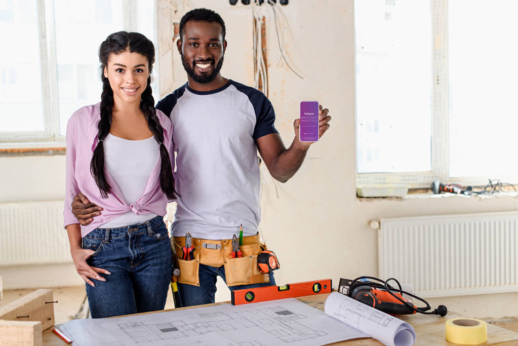 couple holding smartphone with instagram app on screen during renovation - Photo, Image