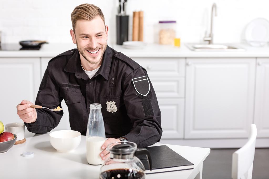usmívající se policista jíst cornflakes s mlékem na kuchyňském stole - Fotografie, Obrázek