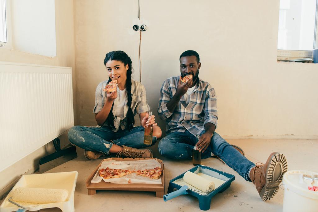 Африканская американская пара ест пиццу и пьет пиво во время ремонта дома
 - Фото, изображение
