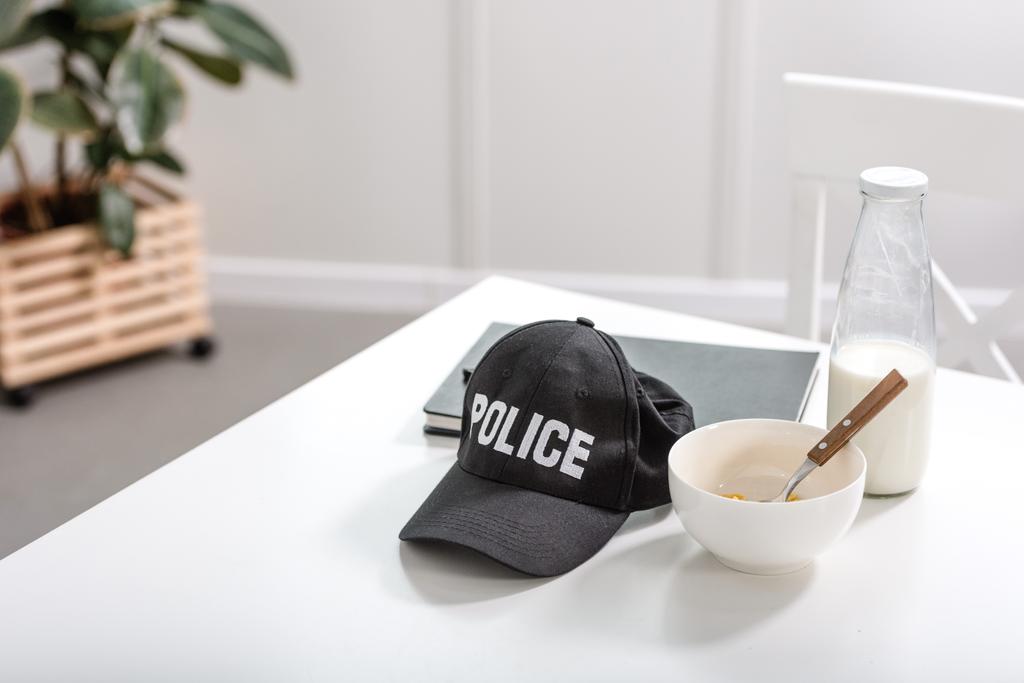 cuaderno, gorra de policía y tazón con desayuno en mesa blanca
 - Foto, Imagen