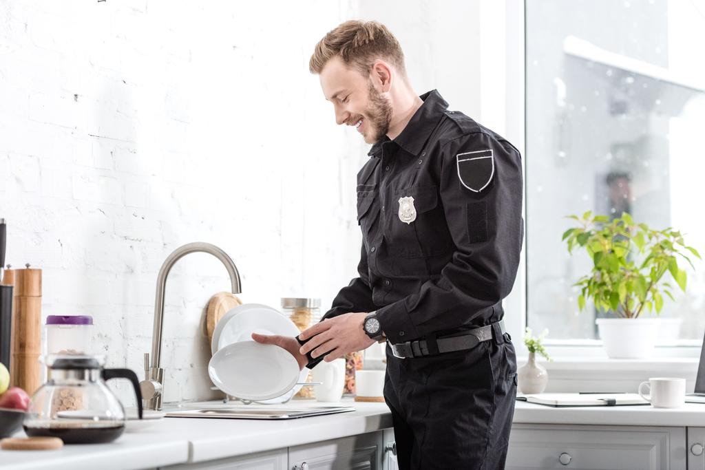 Uśmiechnięty policjant mycia płytkę w kuchni - Zdjęcie, obraz