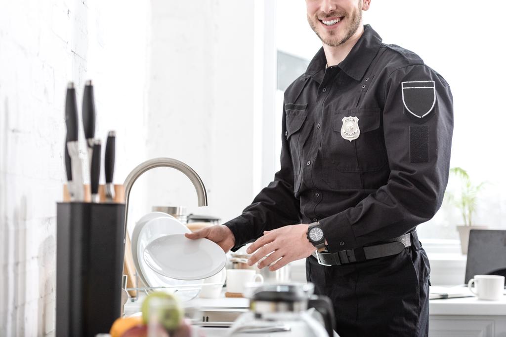 台所で皿を洗うハンサムな警官のトリミング ビュー - 写真・画像