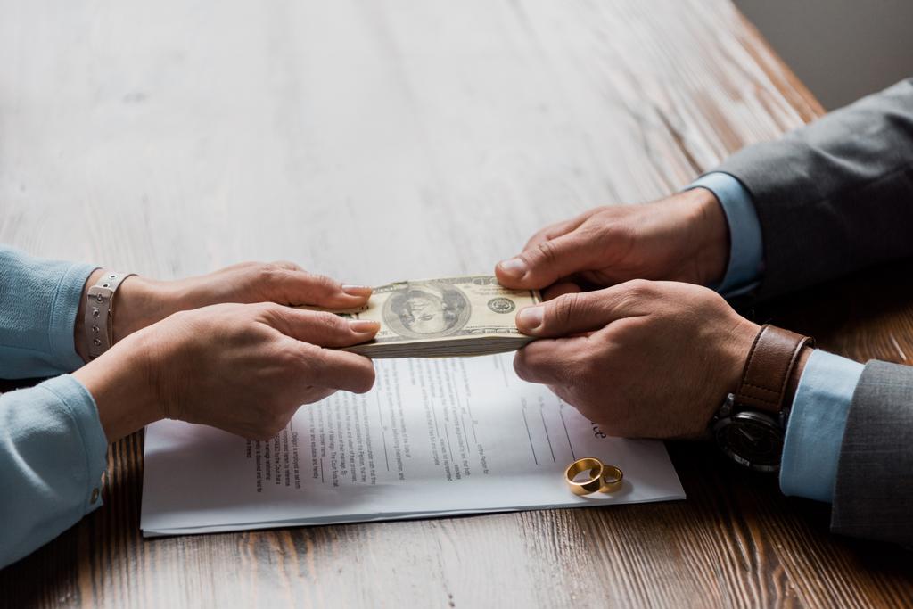 partial view of lawyer and client holding dollar banknotes above divorce decree with wedding rings  - Photo, Image
