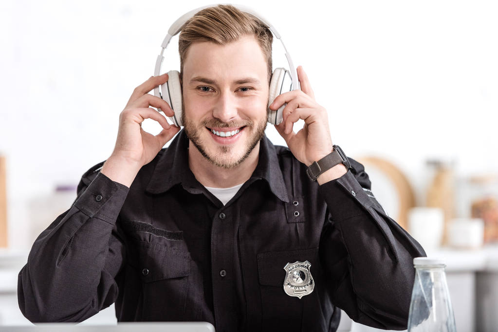 politieagent glimlachend en luisteren naar muziek met een koptelefoon op keuken - Foto, afbeelding