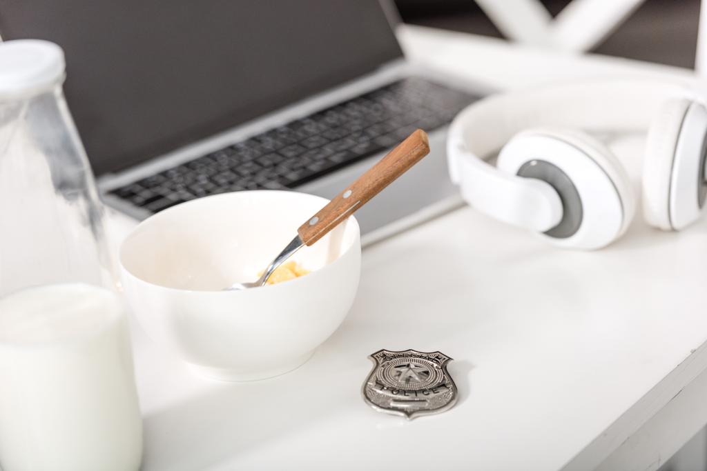 lap-top, ακουστικά, αστυνομική κονκάρδα και μπολ με πρωινό στον άσπρο πίνακα - Φωτογραφία, εικόνα