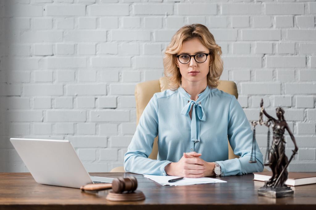 σοβαρή γυναίκα δικηγόρος σε γυαλιά, κάθεται στο χώρο εργασίας και να βλέπουν τα φωτογραφικών μηχανών - Φωτογραφία, εικόνα