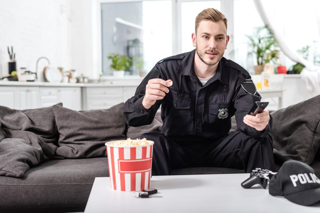 policjant siedzi na kanapie, jedzenie popcorn i oglądając film - Zdjęcie, obraz