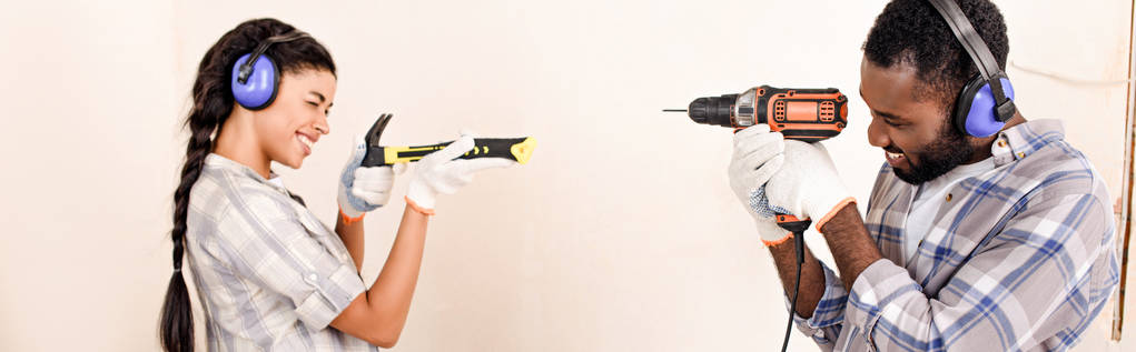 vista lateral do casal em fones de ouvido de proteção se divertindo com ferramentas durante a renovação da casa
 - Foto, Imagem