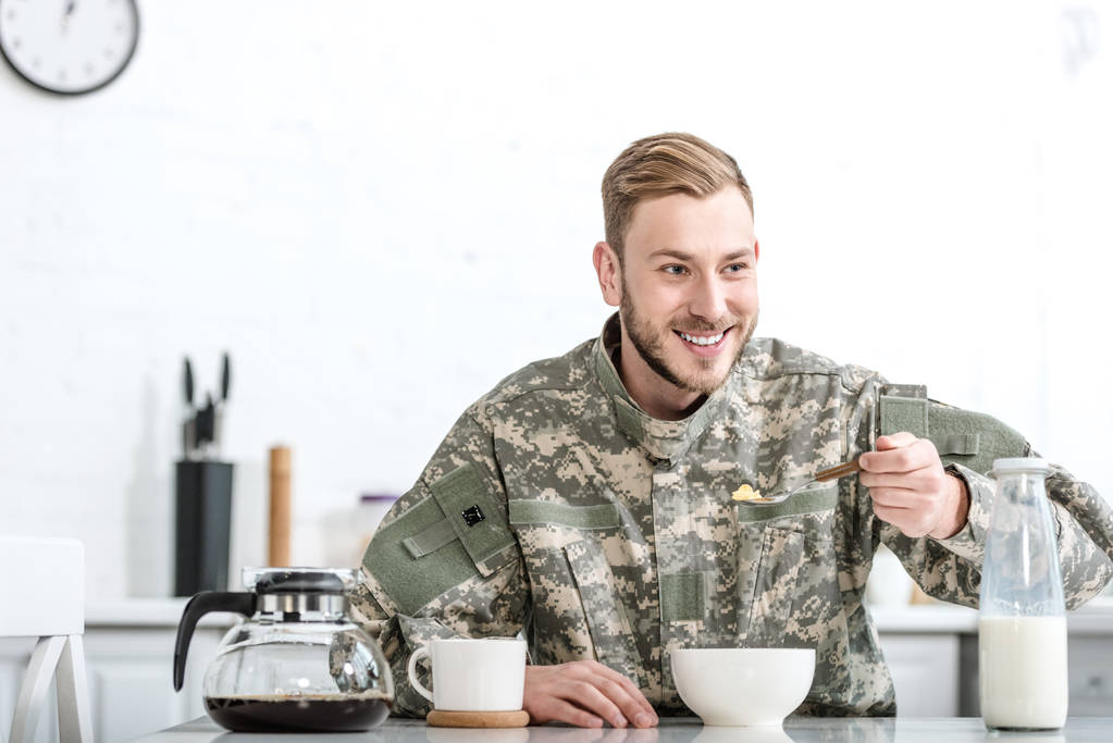 Усміхнений чоловік у військовій формі їсть кукурудзяні пластівці на кухні
 - Фото, зображення