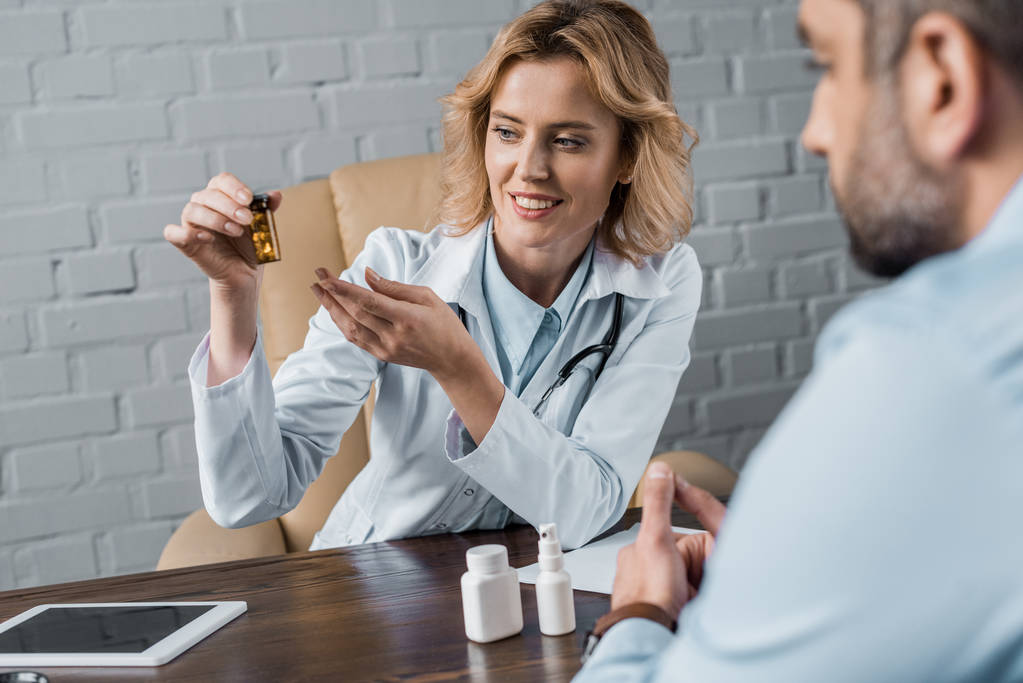 усміхнена жінка-лікар показує банку таблеток для пацієнта в офісі
 - Фото, зображення