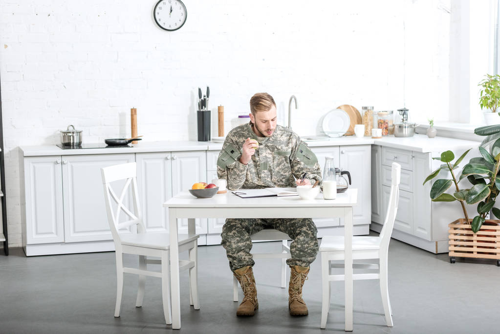 στρατιώτης του στρατού, κάθεται στο τραπέζι της κουζίνας και έχοντας πρωινό στο σπίτι  - Φωτογραφία, εικόνα