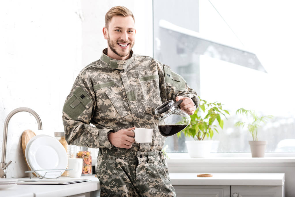 lachende leger soldaat gieten gefilterde koffie in keuken - Foto, afbeelding