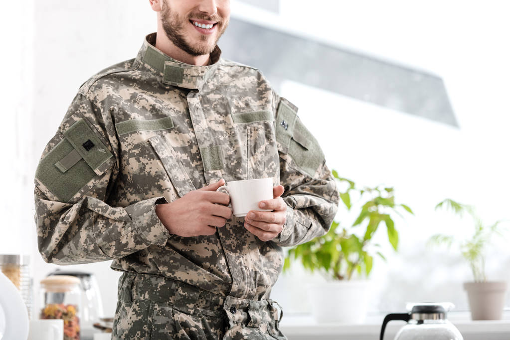 обрізаний вид армійського солдата, що тримає чашку кави на кухні
 - Фото, зображення
