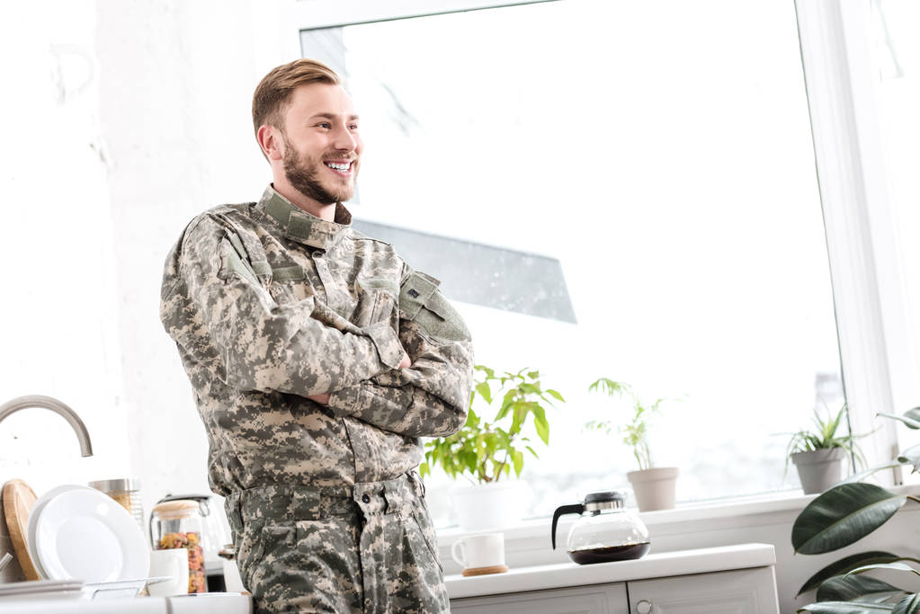 Lächelnder Soldat mit verschränkten Armen in der Küche - Foto, Bild