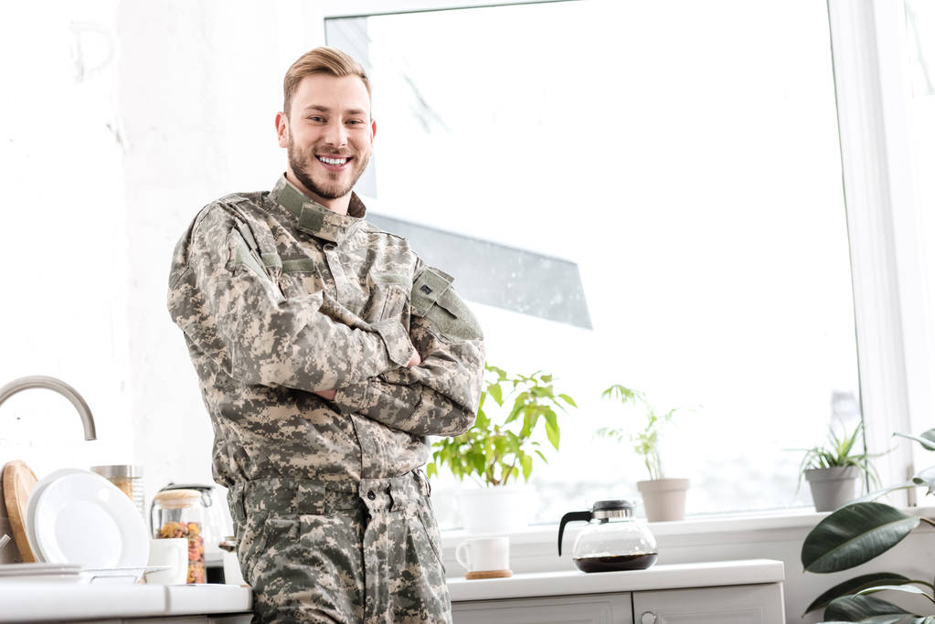 smiling army soldier with arms crossed in kitchen - Photo, Image