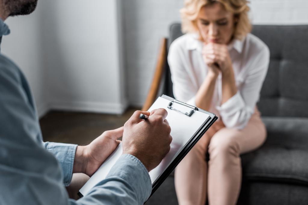 mujer deprimida que tiene sesión de terapia psicológica en el consultorio mientras el terapeuta escribe en portapapeles
 - Foto, imagen