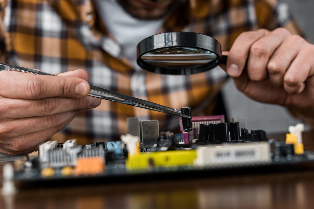 cropped shot of electronics engineer with tweezers and magnifying glass repairing motherboard - Photo, Image