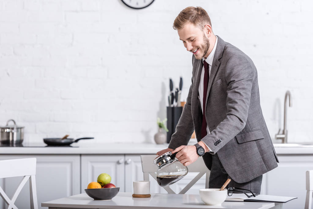 χαμογελώντας επιχειρηματίας έκχυση φιλτραρισμένο καφέ στο φλυτζάνι στην κουζίνα - Φωτογραφία, εικόνα