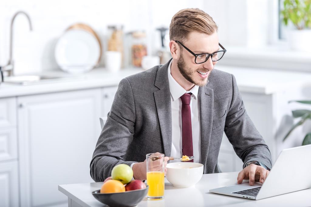 empresário trabalhando no laptop enquanto toma café da manhã na cozinha
 - Foto, Imagem