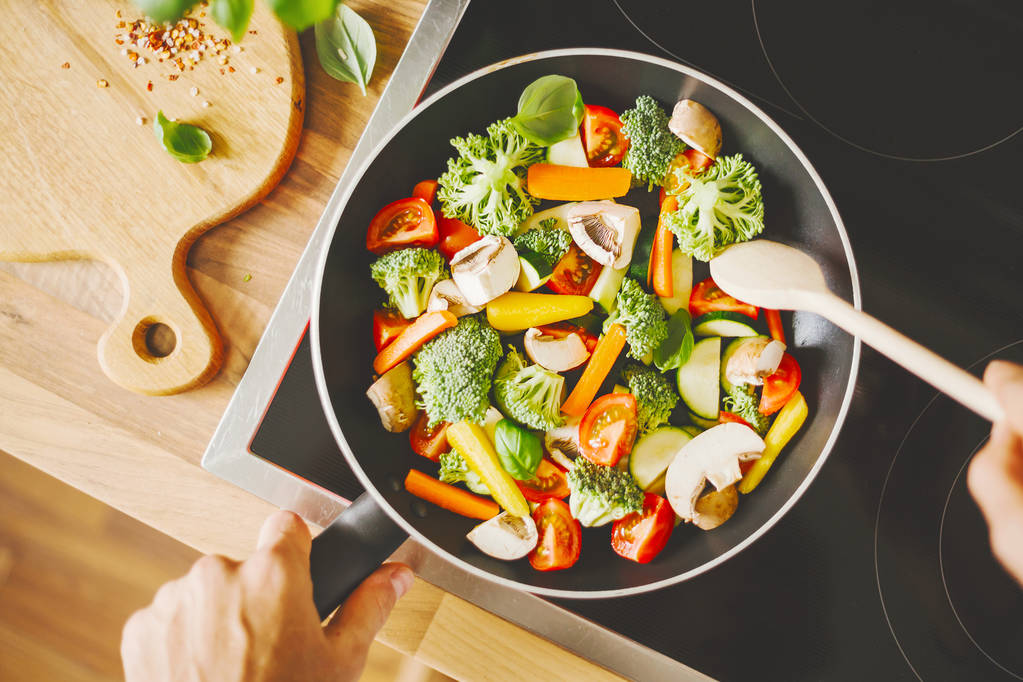 bijgesneden schot van man frituren verse gezonde groenten in de pan op inductie kookplaat - Foto, afbeelding