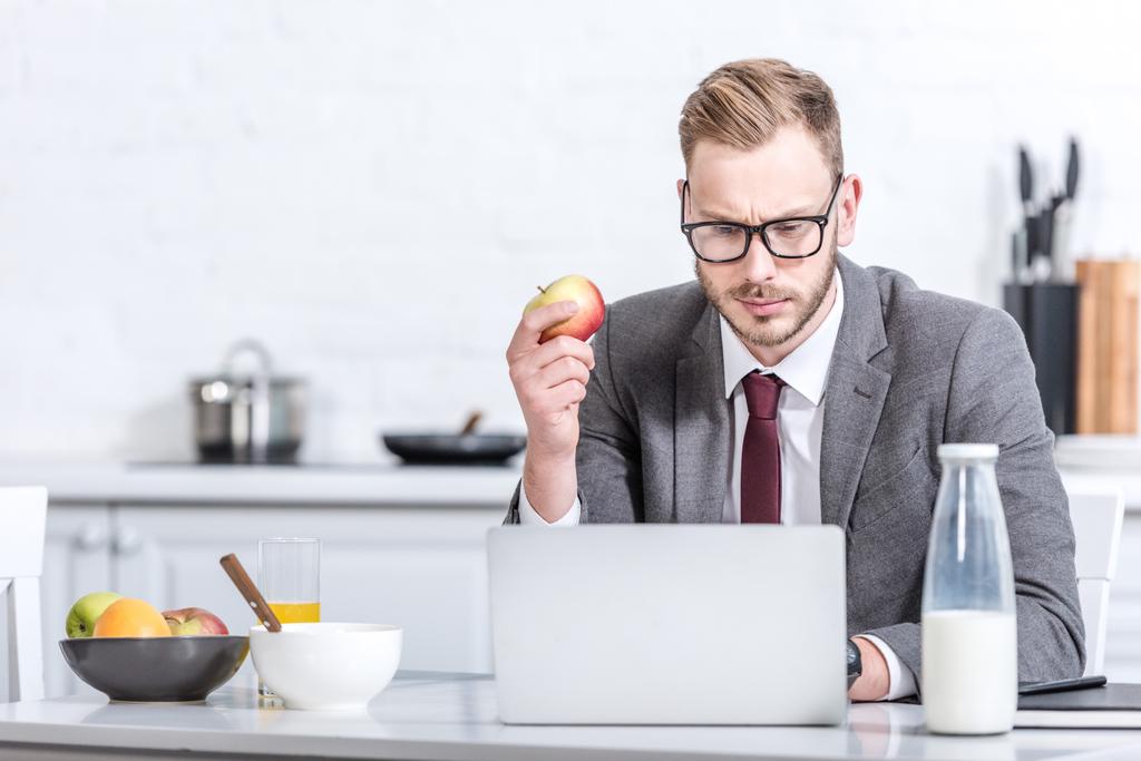 homme d'affaires travaillant sur ordinateur portable tout en mangeant des pommes à la cuisine
 - Photo, image