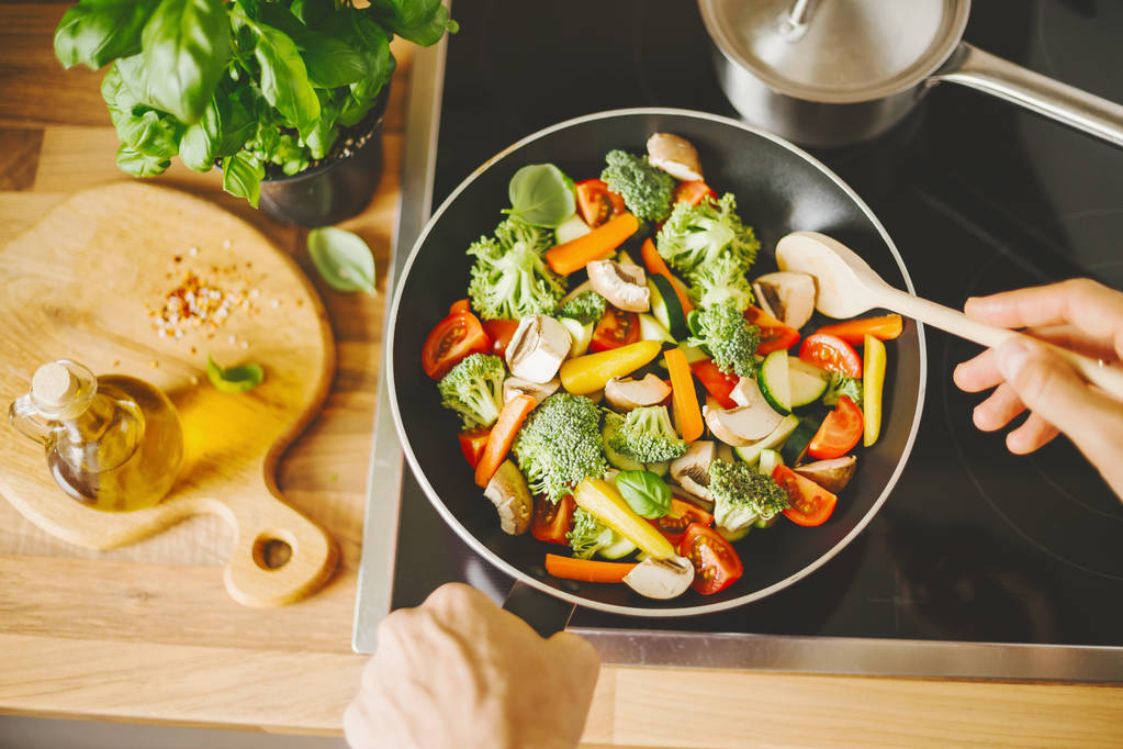 вид зверху людини смажать свіжі здорові овочі з сковородою на індукційній плиті
 - Фото, зображення