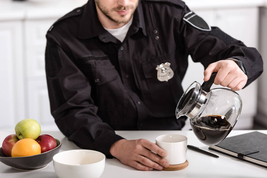 vista recortada del oficial de policía vertiendo café filtrado de maceta de vidrio en la cocina por la mañana
 - Foto, imagen
