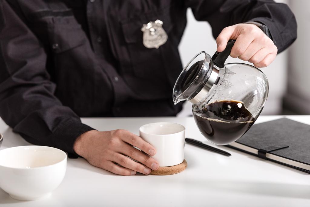 rajattu näkymä poliisi kaatamalla suodatettua kahvia lasipannusta keittiön pöydässä
 - Valokuva, kuva