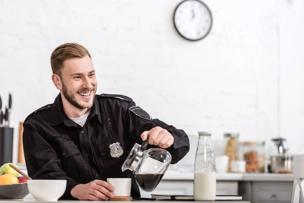 ευτυχισμένος αξιωματικός της αστυνομίας που ρίχνει το φιλτραρισμένο καφέ από γυάλινο δοχείο στην κουζίνα - Φωτογραφία, εικόνα