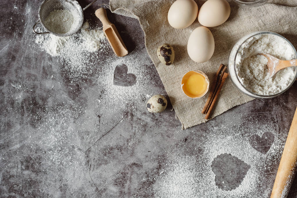 gesunde Backzutaten. Hintergrund mit Mehl, Nudelholz, Eiern und Herzform auf einem grauen Küchentisch. Draufsicht für Valentinstag Kochen. Kopierraum. - Foto, Bild