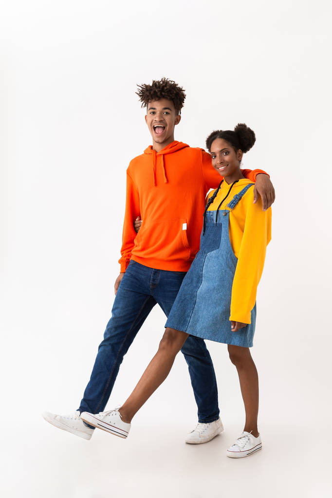 Pleine longueur photo de couple afro-américain adolescent en vêtements colorés souriant tout en marchant ensemble isolé sur fond blanc
 - Photo, image