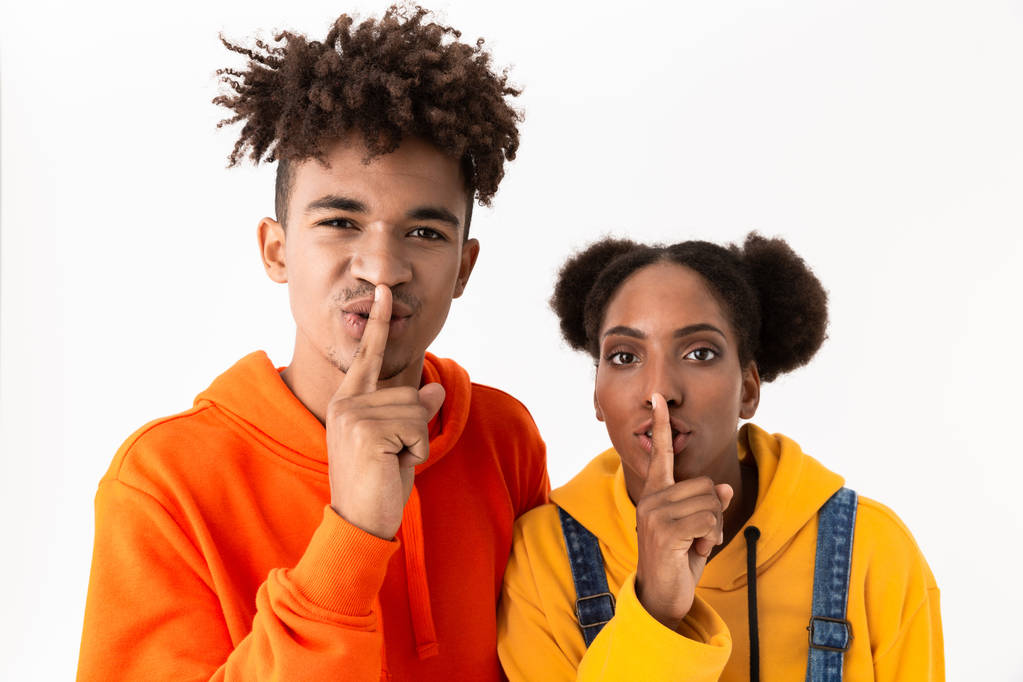 Imagen de hermano y hermana afroamericanos en ropa colorida sosteniendo los dedos en la boca aislados sobre fondo blanco
 - Foto, Imagen