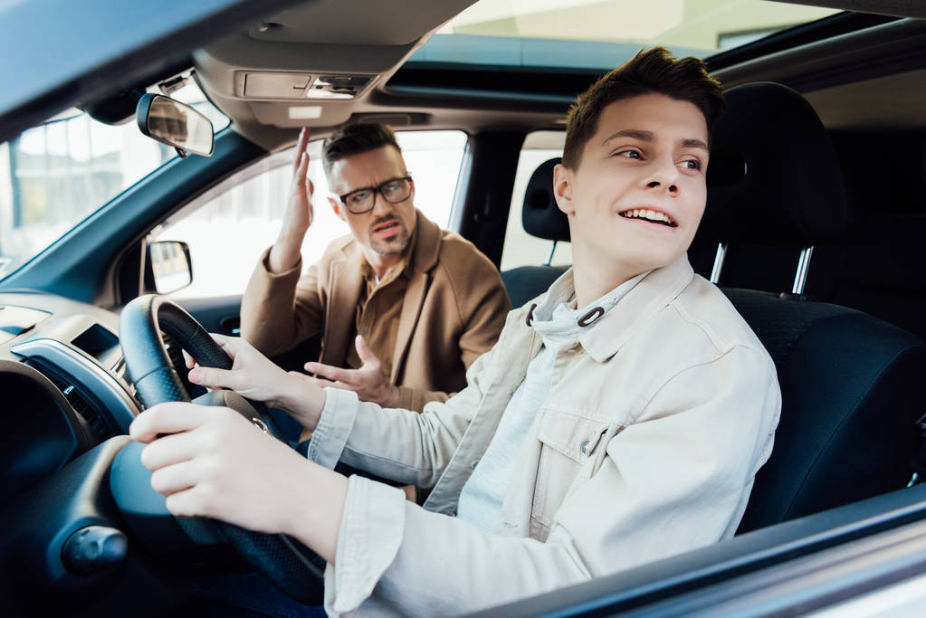 irritated father teaching smiling teen son driving car - Photo, Image