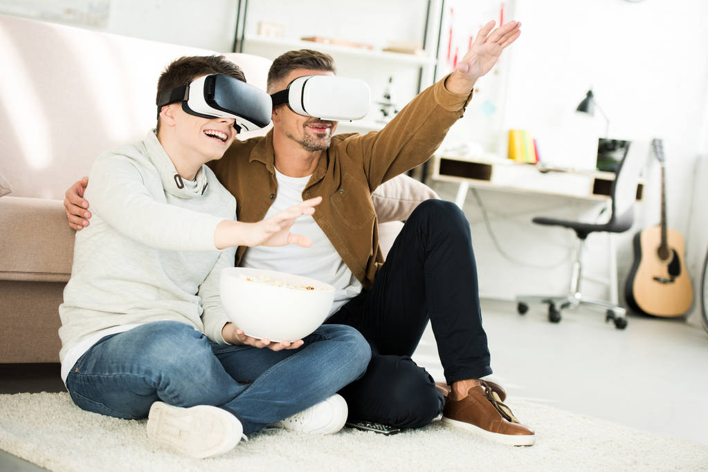 father and teen son watching something with virtual reality headsets at home - Photo, Image