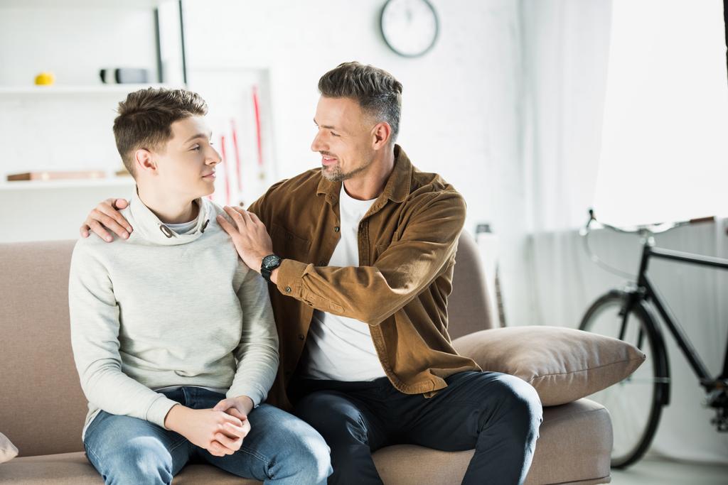 father hugging teen son on sofa at home - Photo, Image