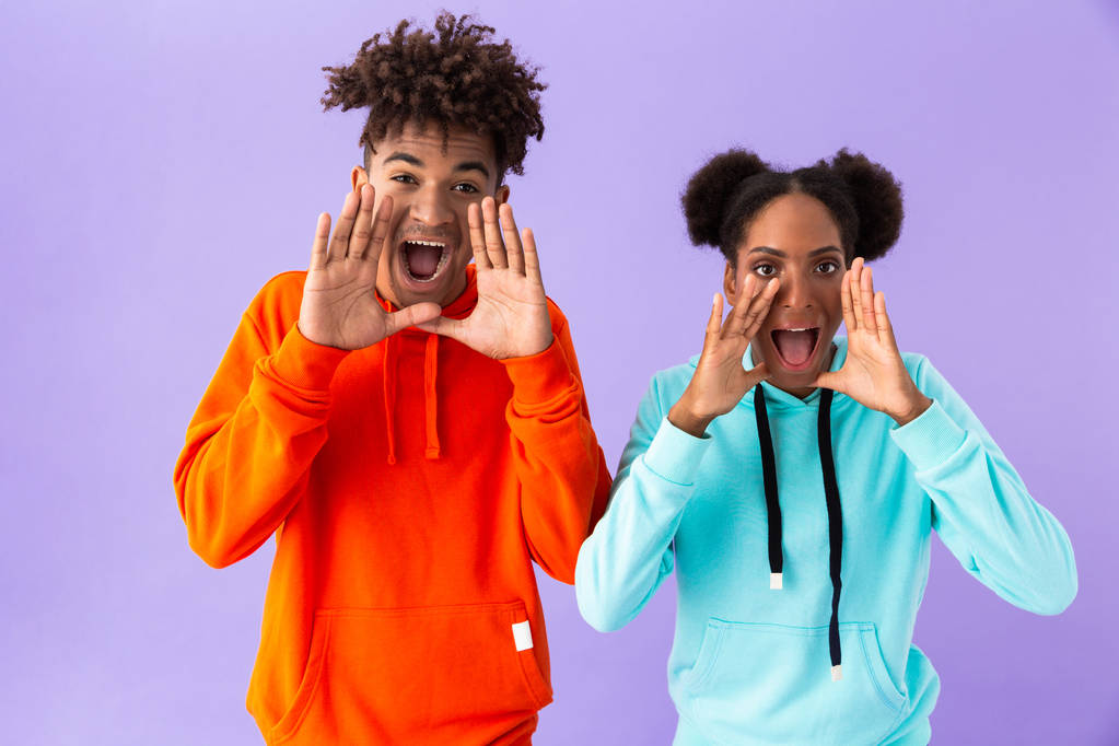 Foto von attraktiven afrikanisch-amerikanischen Paar schreit oder ruft mit den Händen im Gesicht isoliert über violetten Hintergrund - Foto, Bild
