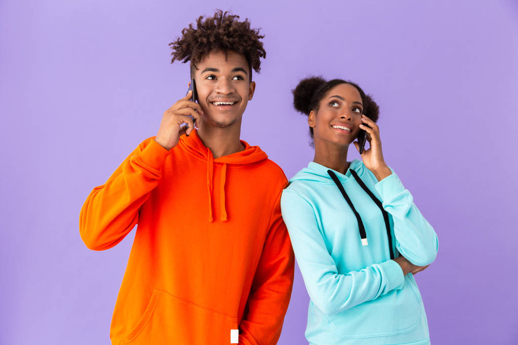 Foto van vrolijke Afro-Amerikaanse jongen en meisje samen praten op mobiele telefoon geïsoleerd over violette achtergrond - Foto, afbeelding