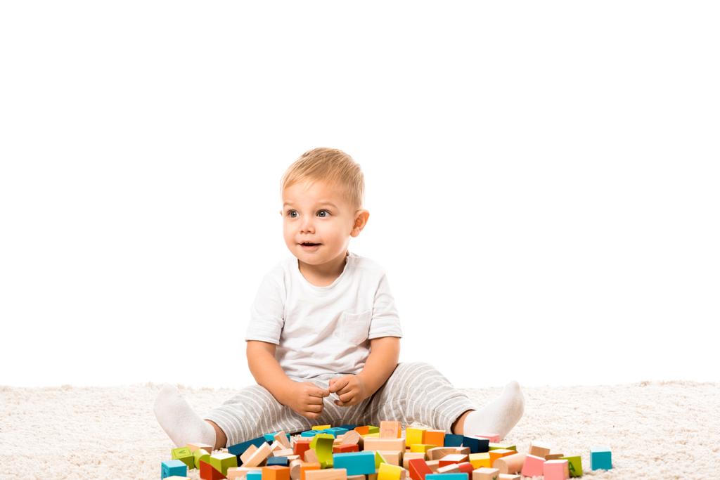 bambino sorridente seduto su tappeto e giocare con blocchi di legno multicolore isolati su bianco
 - Foto, immagini