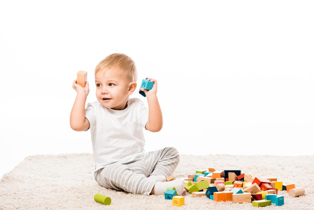 schattig jongetje spelen met houten blokken op tapijt geïsoleerd op wit - Foto, afbeelding