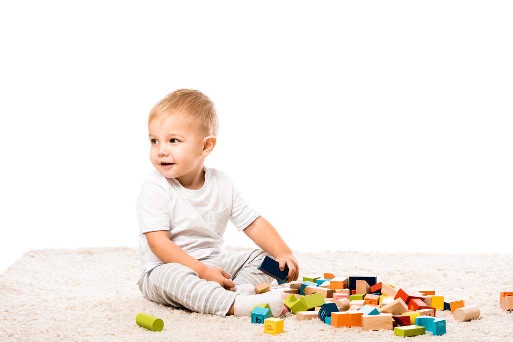 mignon tout-petit garçon souriant et jouant avec des blocs en bois sur tapis isolé sur blanc
 - Photo, image