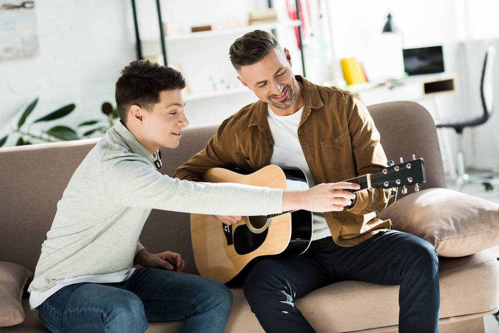 teen son teaching father play acoustic guitar at home - Photo, Image