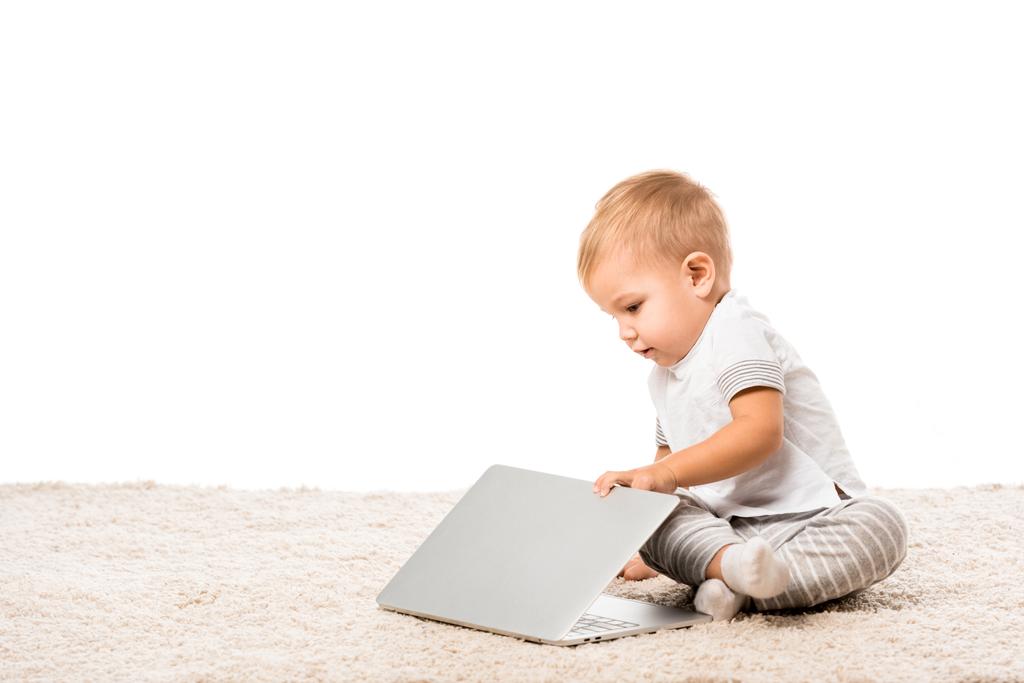 Kleinkind sitzt auf Teppich und schließt Laptop isoliert auf weißem Grund - Foto, Bild