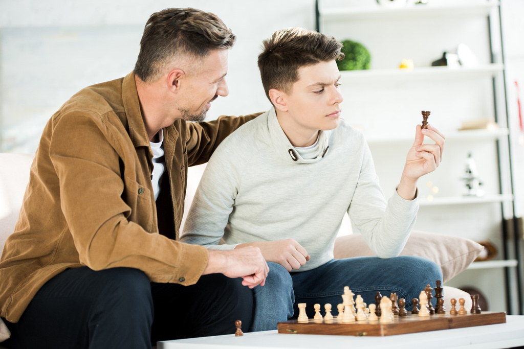 father hugging teen son while he looking at chess figure at home - Photo, Image