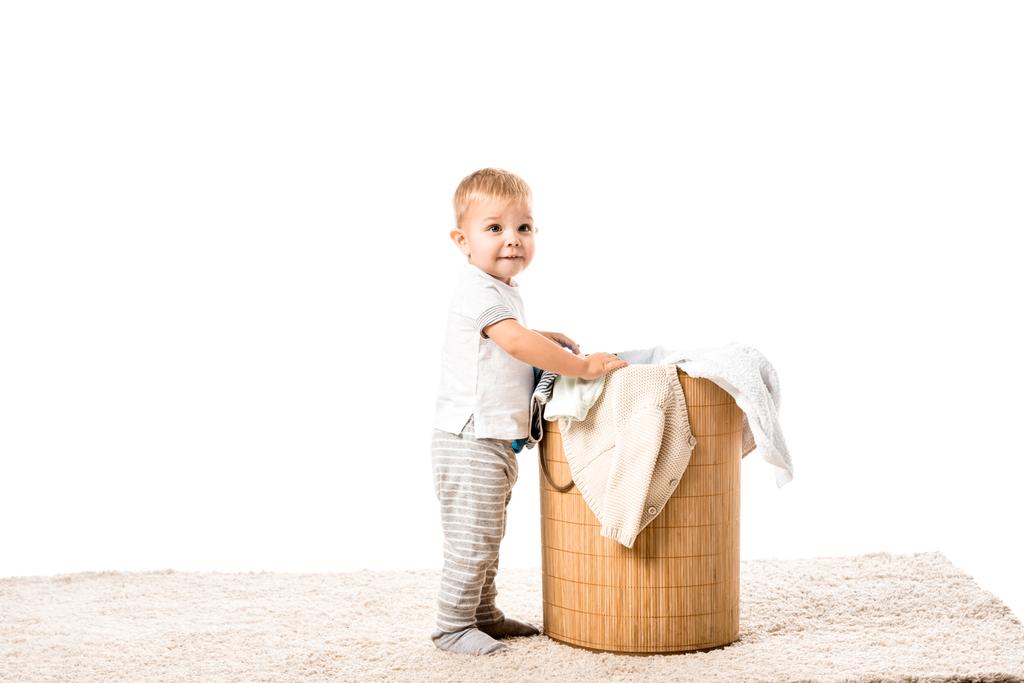 menino criança de pé na frente de cesta de lavandaria de vime e sorrindo isolado no branco
 - Foto, Imagem