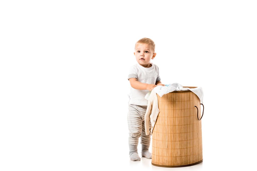 nice toddler boy standing near wicker laundry basket isolated on white - Photo, Image
