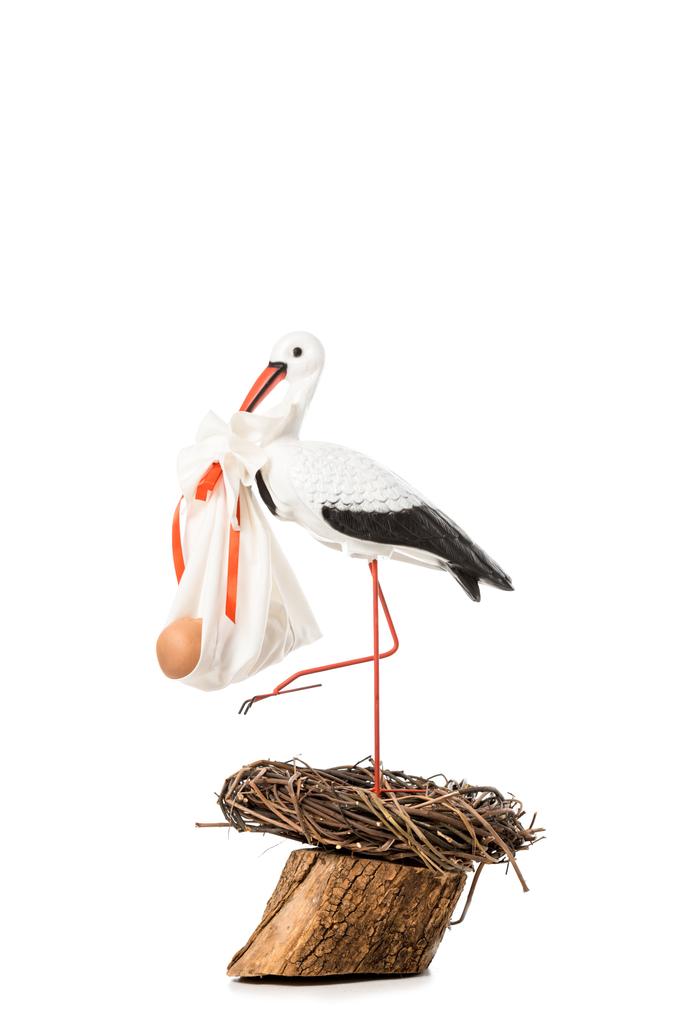 cegonha decorativa segurando bebê fralda com boneca e em pé no ninho de vime isolado no branco
 - Foto, Imagem