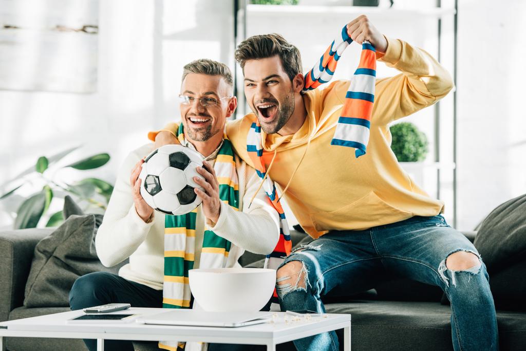 ενθουσιασμένος ο γιος και πατέρας του ώριμη με φουλάρια που παρακολουθούν ποδόσφαιρο και ουρλιάζοντας στο σπίτι - Φωτογραφία, εικόνα