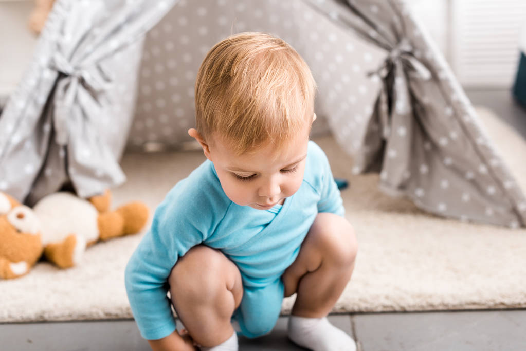 灰色ウィグワム近くしゃがみ込んに座っているブルーのボディー スーツでかわいい幼児の少年 - 写真・画像